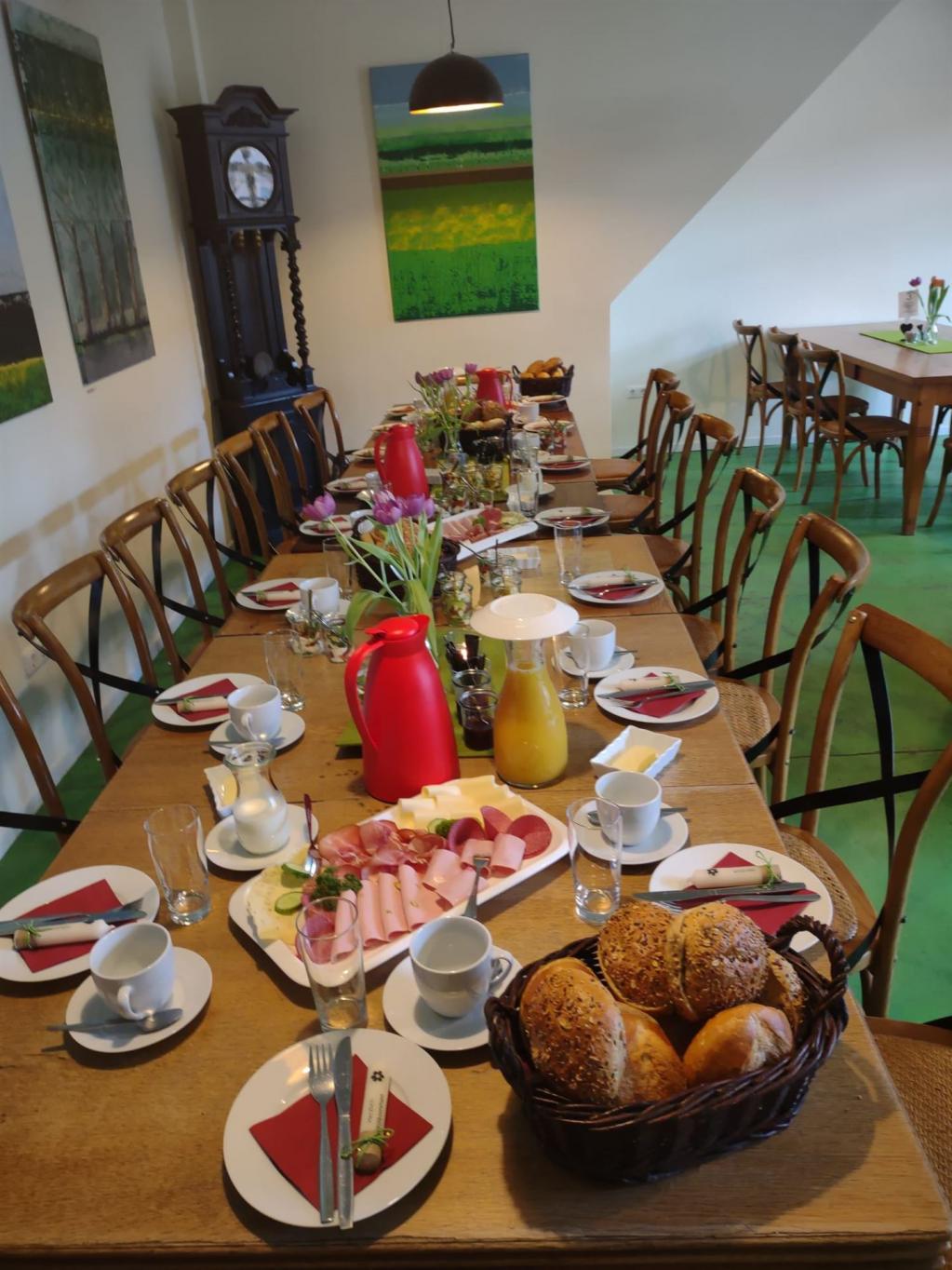 Langer gedeckter Esstisch mit Geschirr, Brötchen, Aufschnitt und Getränken in einem Esszimmer